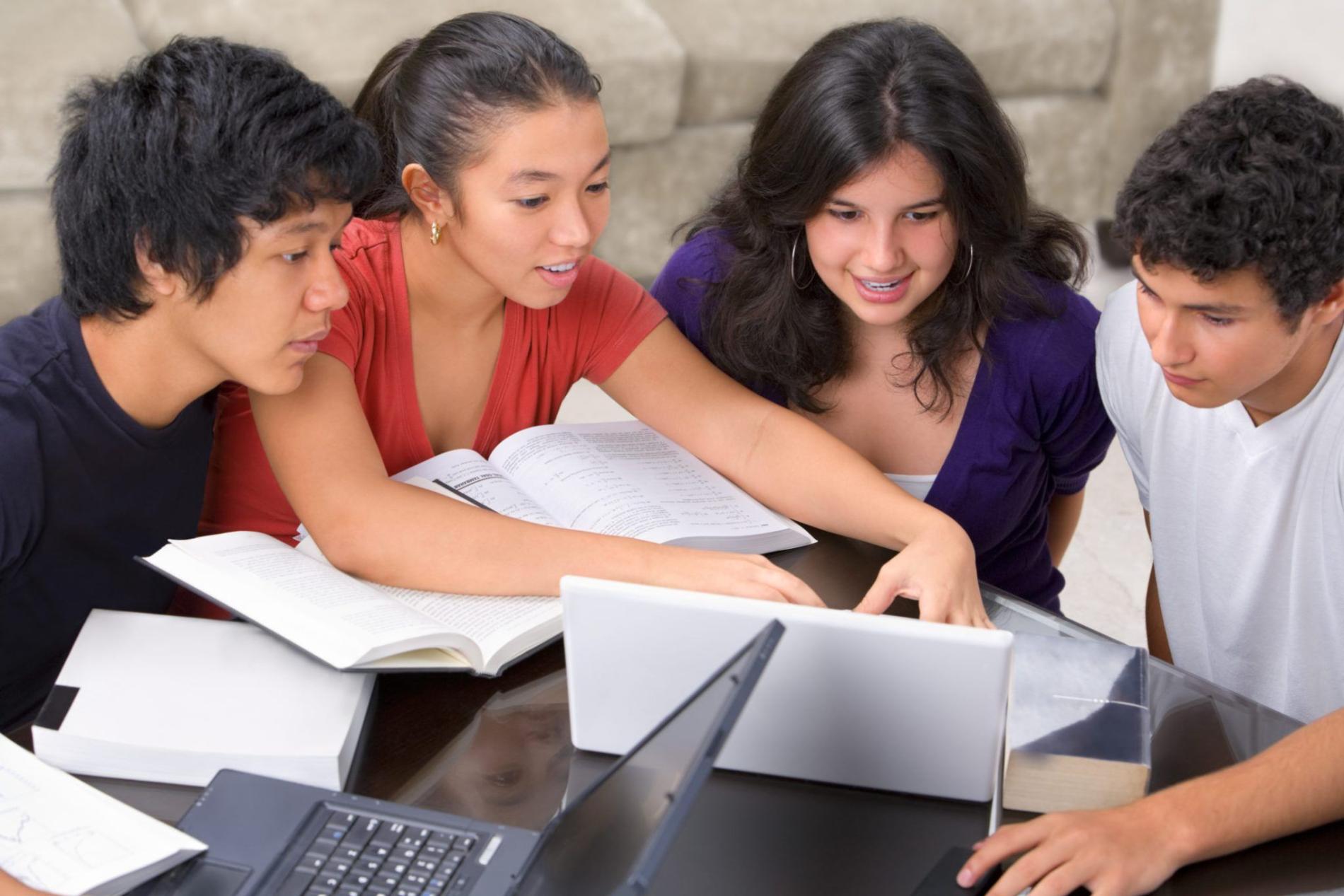 Four students working together over books and a laptop